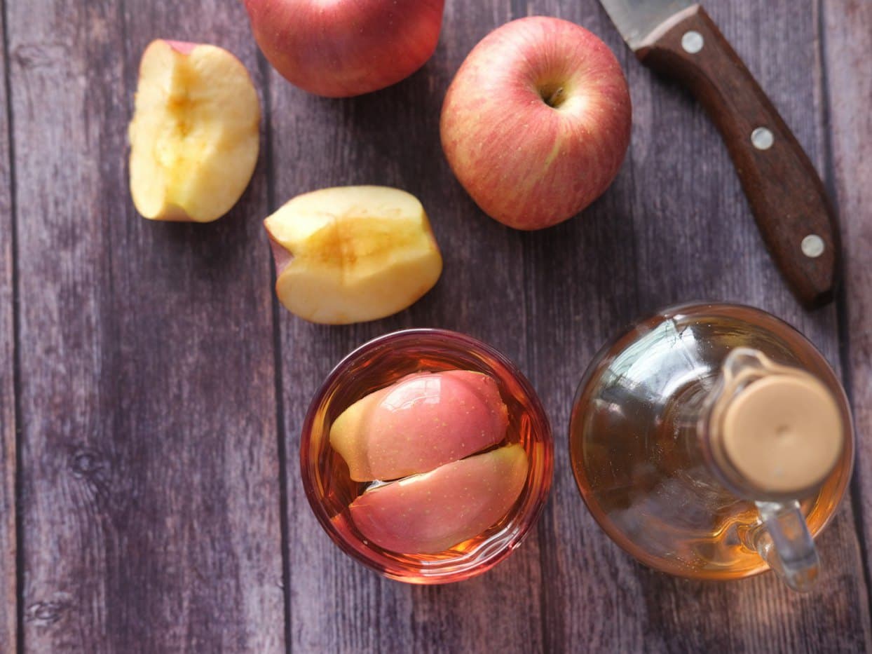 Red apples, apple slices and a glass bottle of apple cider vinegar on a wooden table
